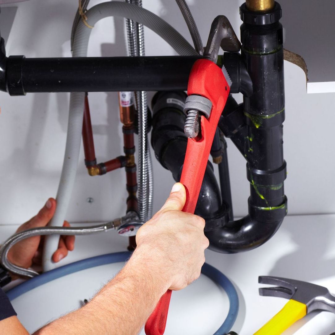 A man is fixing a sink with a red wrench