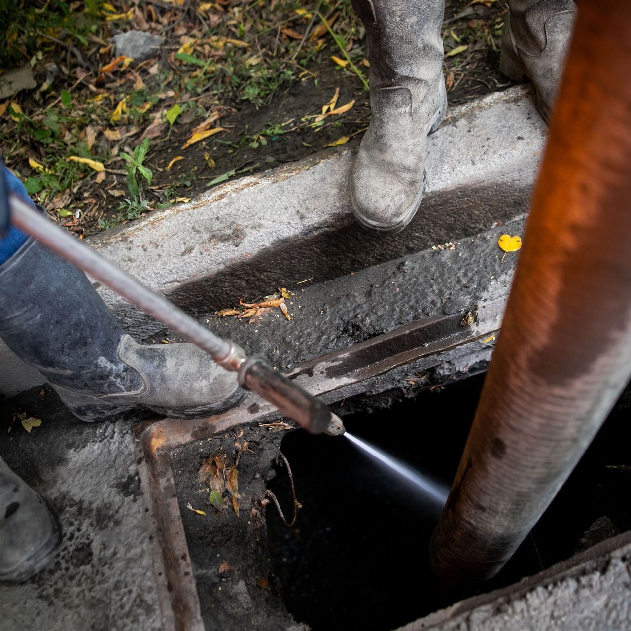 A person is using a hose to clean a drain