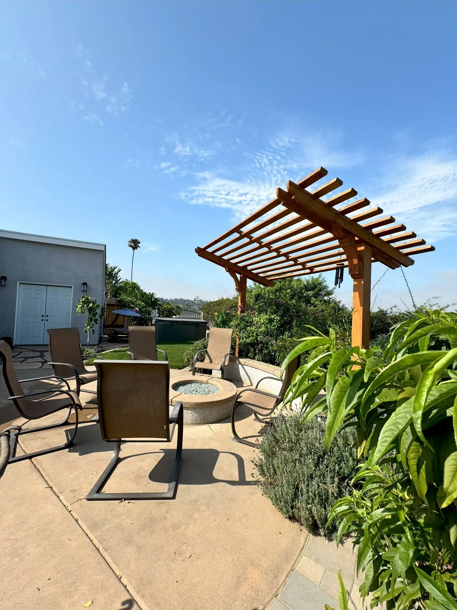 Patio with a pergola, fire pit, and seating under a bright blue sky.