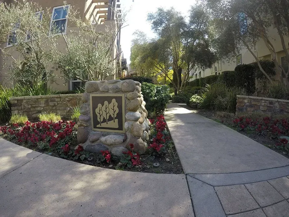 Sign for a residential area with stone pillars, a pathway, and landscaping with red flowers.
