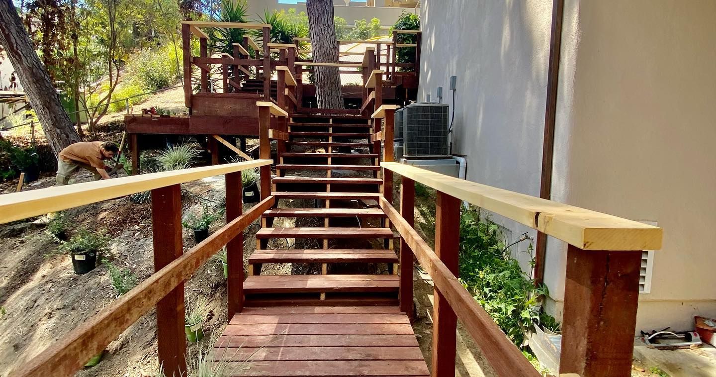 Wooden stairs with railings leading up to a deck, set in a hillside landscape.