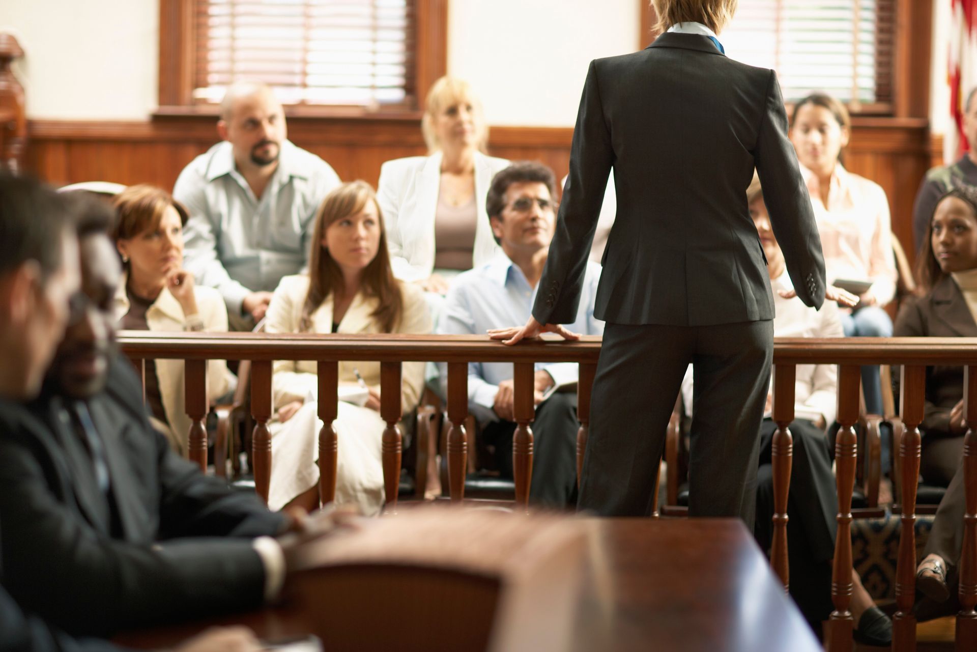 Speaker addressing seated audience in a courtroom-like room with wooden benches and warm light