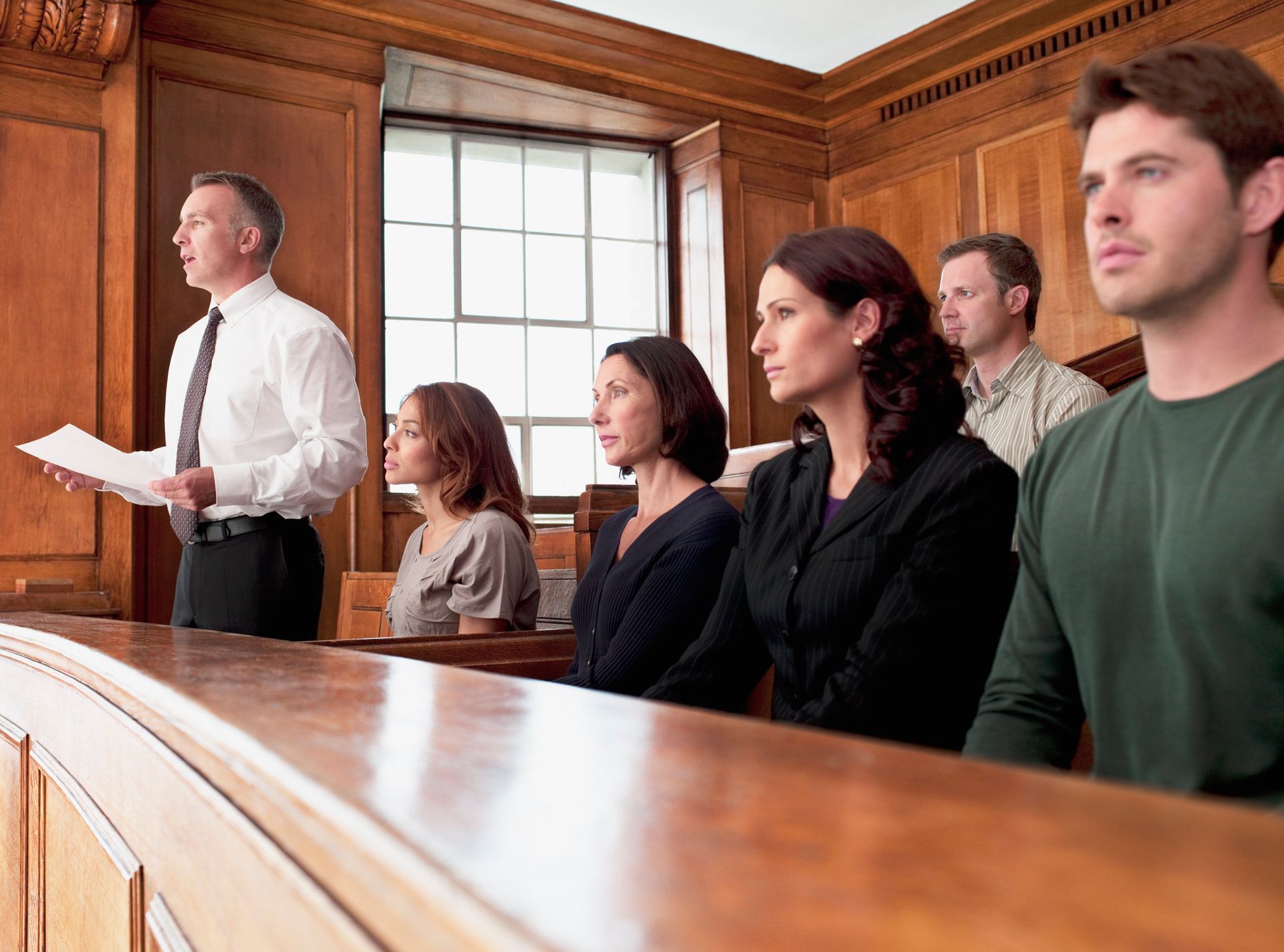 People seated in a courtroom, listening as a man speaks at the front.