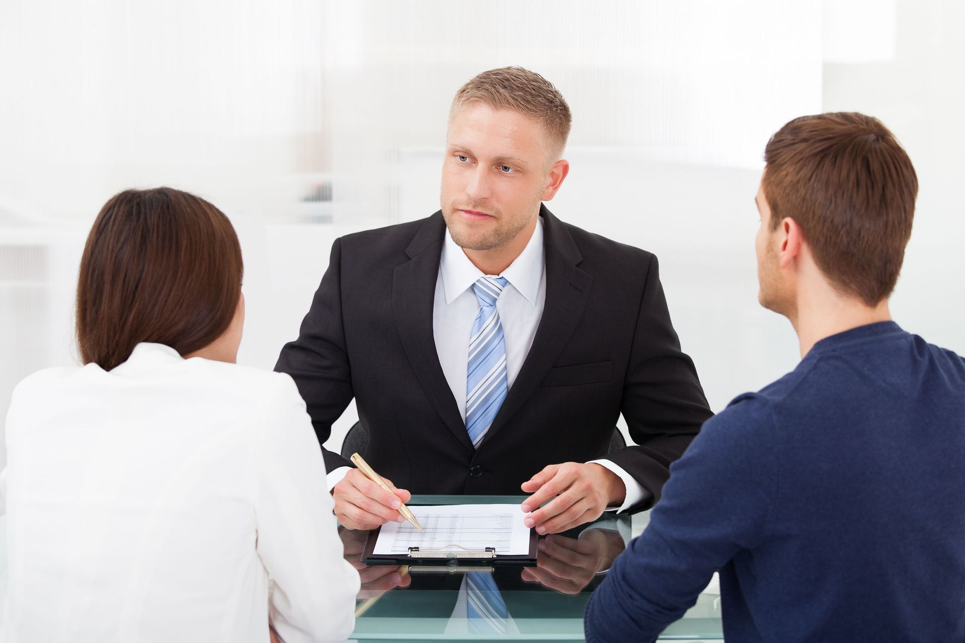 Three people in a business meeting across a glass table, discussing a document in a bright office