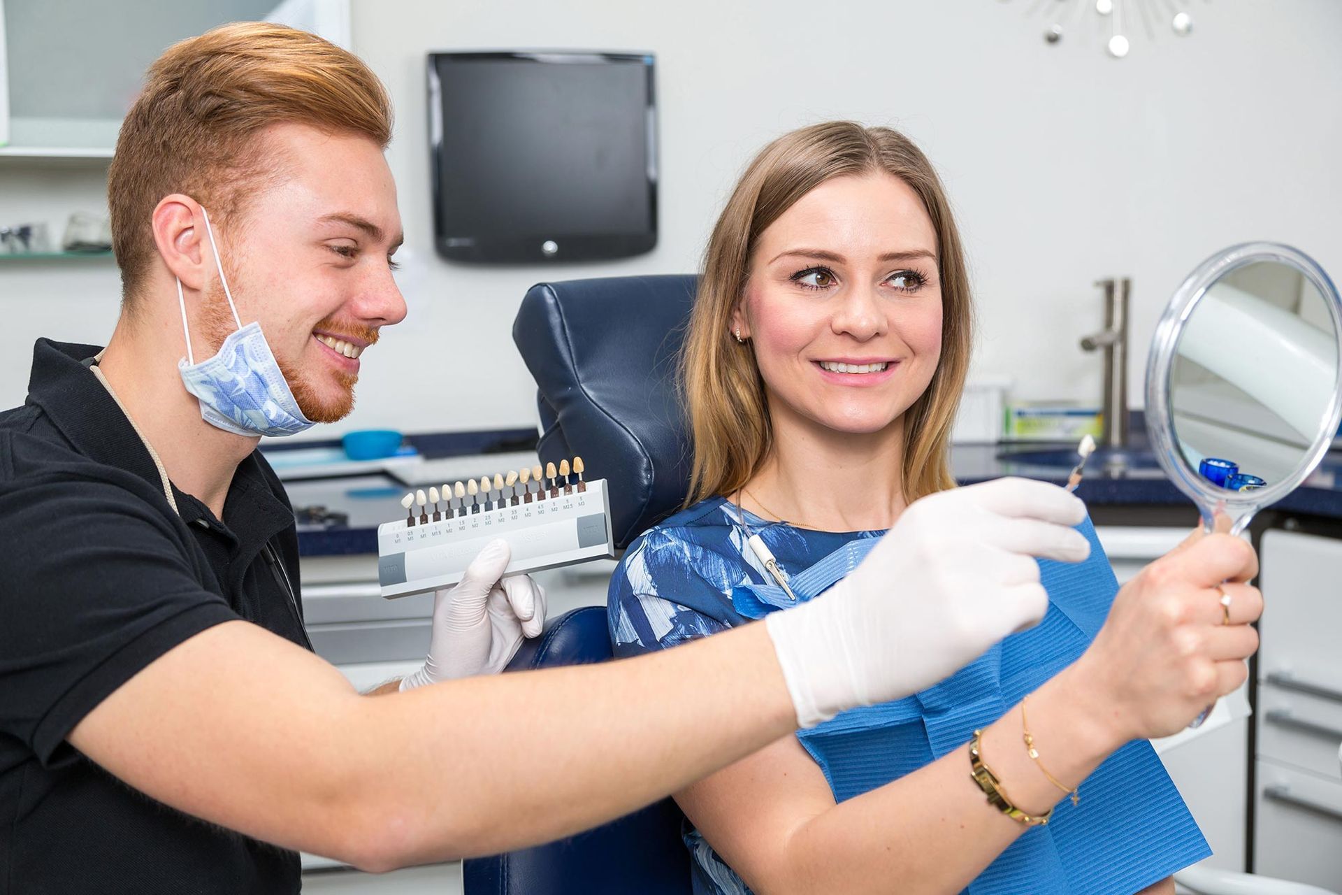 A dentist is looking at a woman 's teeth in a mirror.