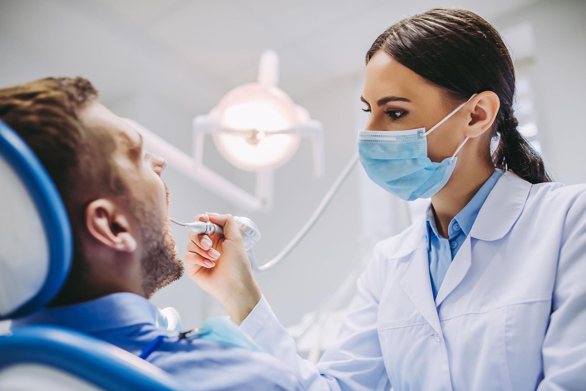 A female dentist is examining a man 's teeth in a dental office.
