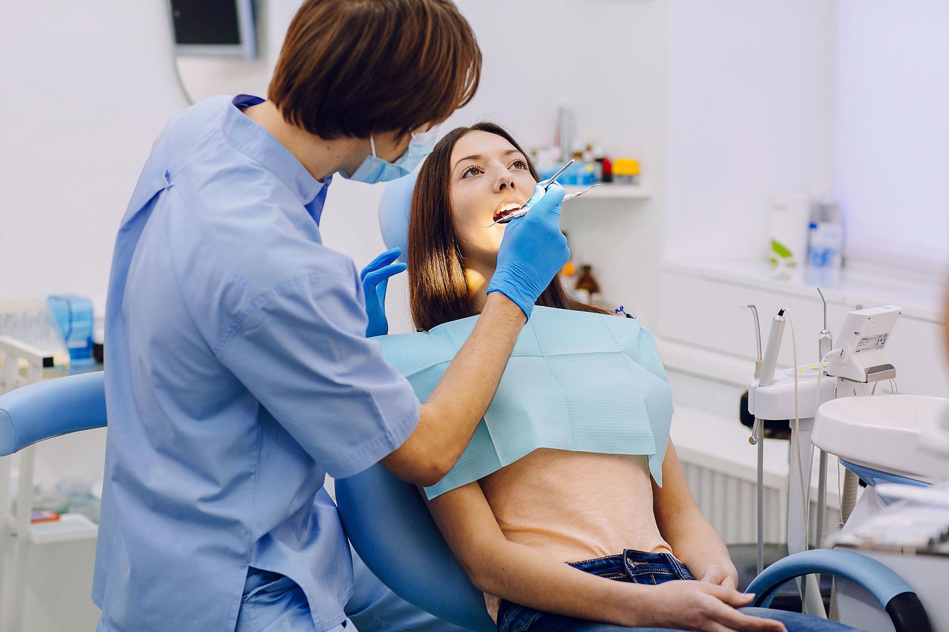 A woman is sitting in a dental chair while a dentist examines her teeth.