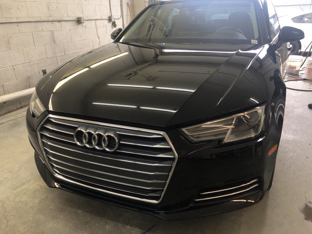 Black Audi sedan parked inside, front view. Grille with the Audi logo. Shiny exterior.