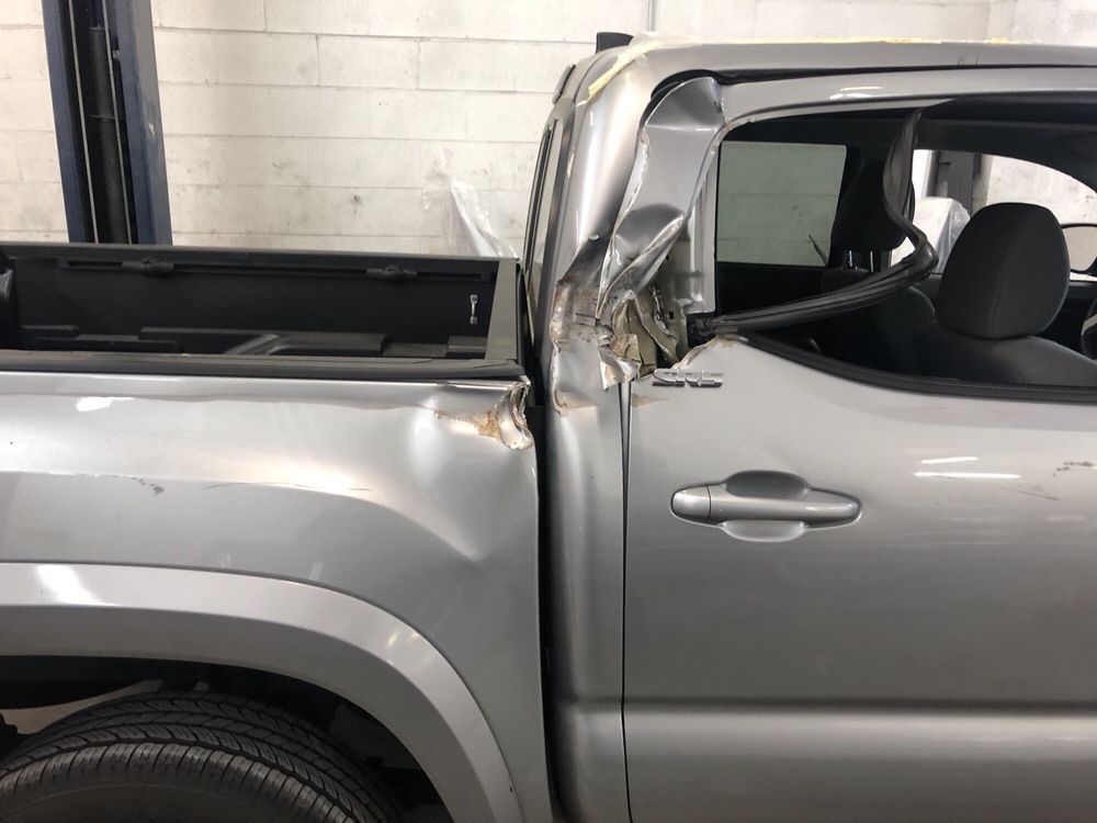 Damaged silver pickup truck cab with crumpled pillar and dents, likely from a collision.