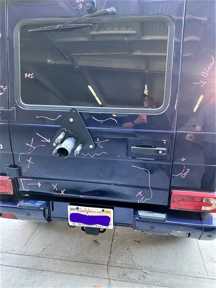 Dark blue SUV rear with modified spare tire carrier and window. California license plate and bumper present.