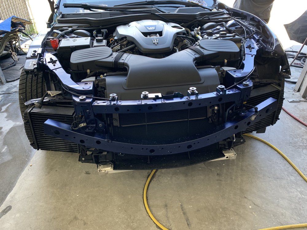 Blue Maserati with front bumper removed, revealing engine components and radiators.