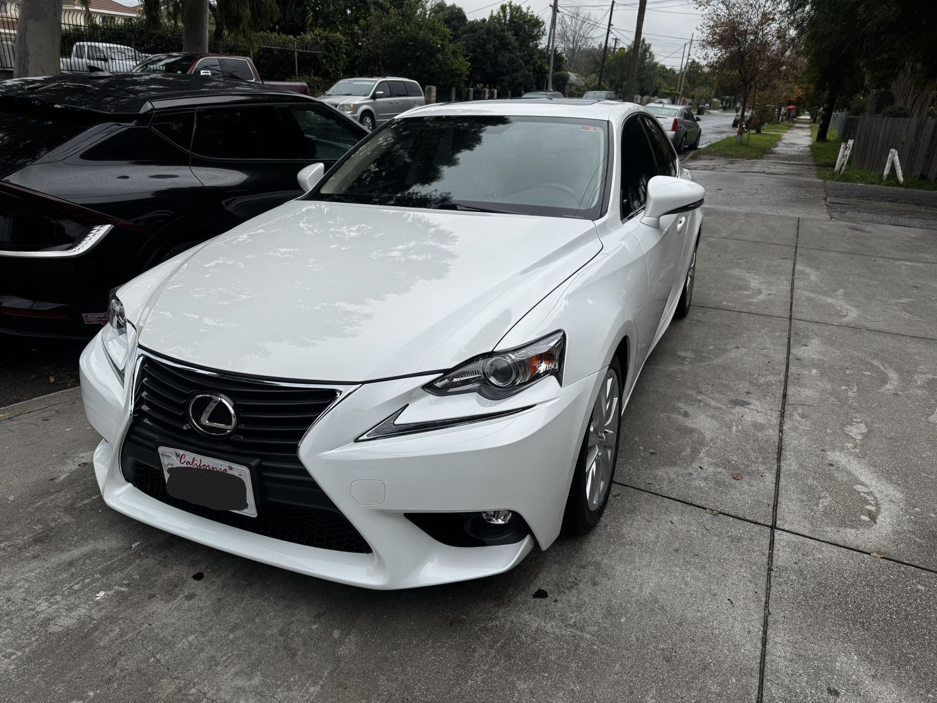 White Lexus sedan parked on a concrete surface. Another black car is beside it. Cloudy day.