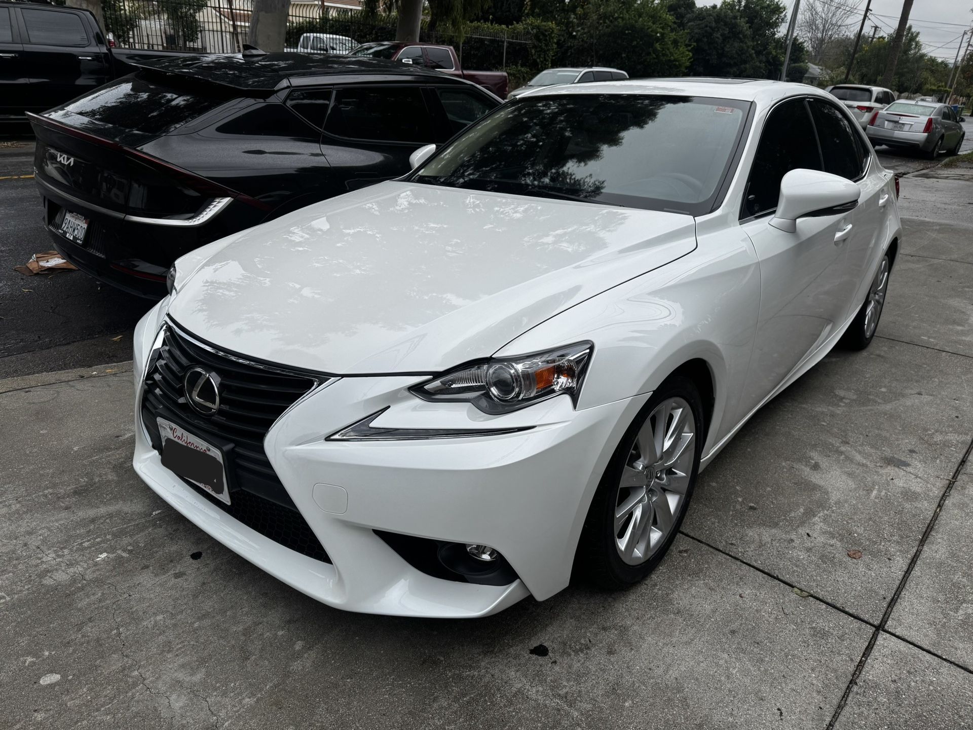 White Lexus sedan parked on a paved lot; other cars are in the background.