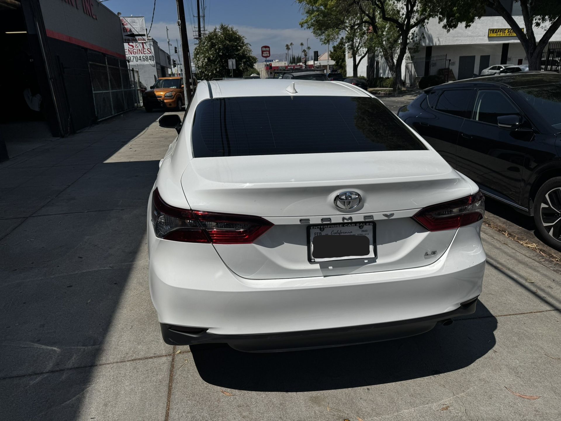 White Toyota Camry parked on a city street; tail lights, license plate visible.