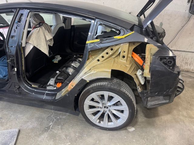 A damaged black Tesla car in a repair shop with its rear side partially dismantled.