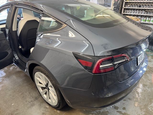 Gray Tesla sedan with rear door open, parked indoors.