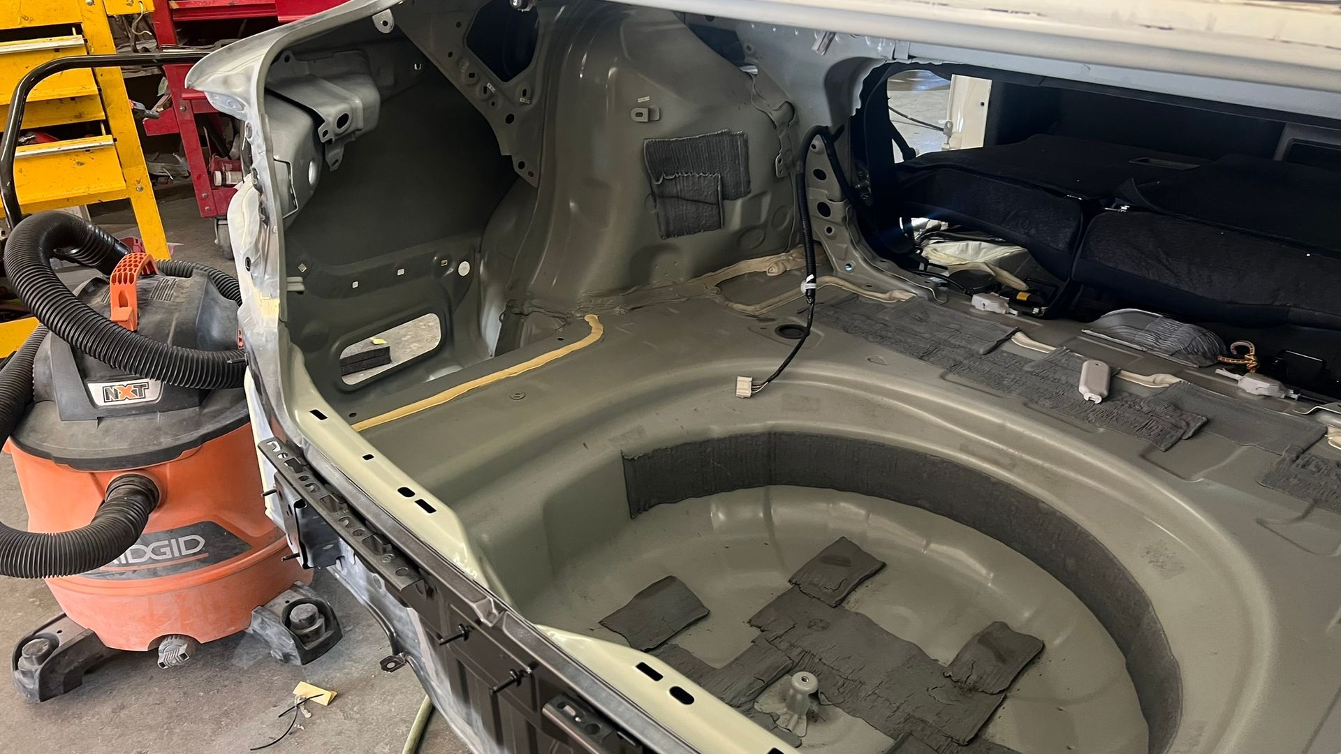 Interior of a car trunk with damage being repaired. Gray metal frame with a shop vacuum.