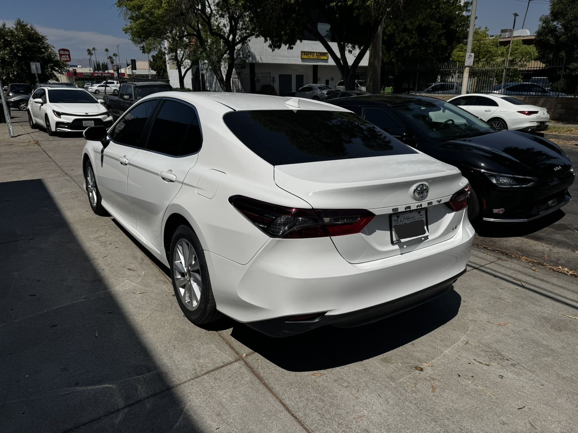 White Toyota Camry parked on a sunny city street next to a black sedan.
