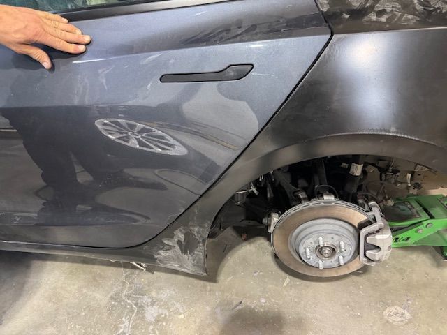 Damaged gray Tesla car door with exposed wheel and brake, being repaired.