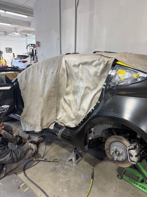 Car being repaired in a garage. Mechanic working on damaged rear panel, covered by protective cloth.