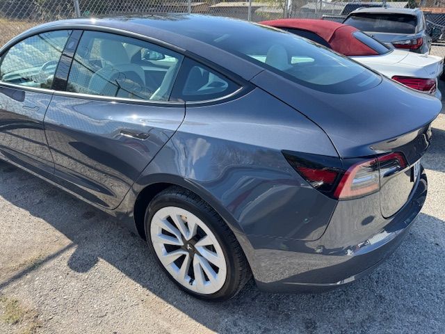 Dark gray Tesla sedan parked outdoors with white-covered wheels, visible rear and side profiles.