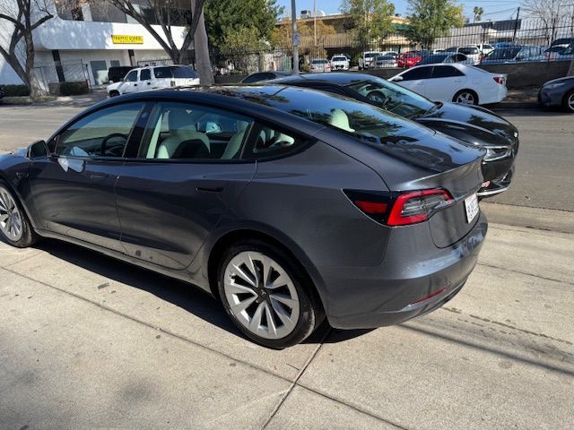 Gray Tesla Model 3 parked on the street next to other vehicles on a sunny day.