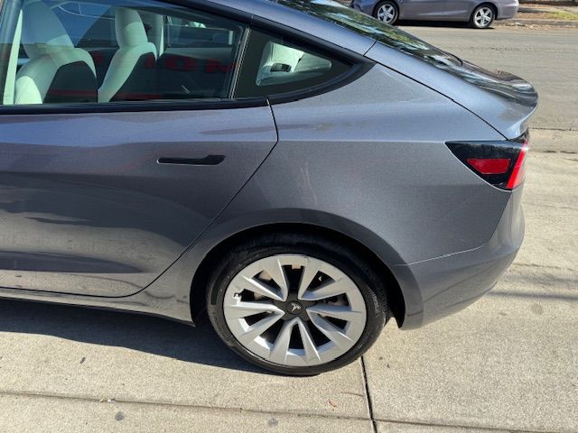Gray Tesla Model 3 car parked on a sidewalk.