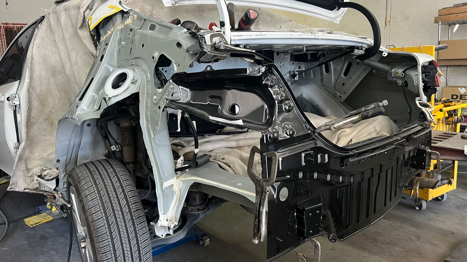 Car frame being repaired in a shop, showing bodywork and exposed metal components.