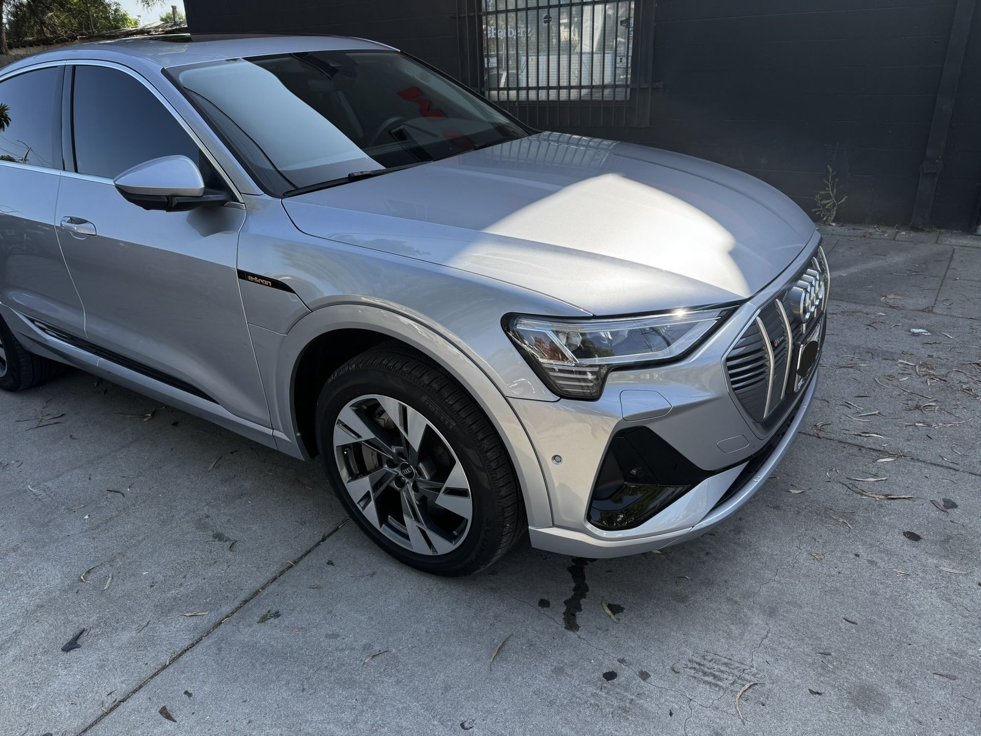 Silver Audi e-tron SUV parked on concrete next to a dark building.