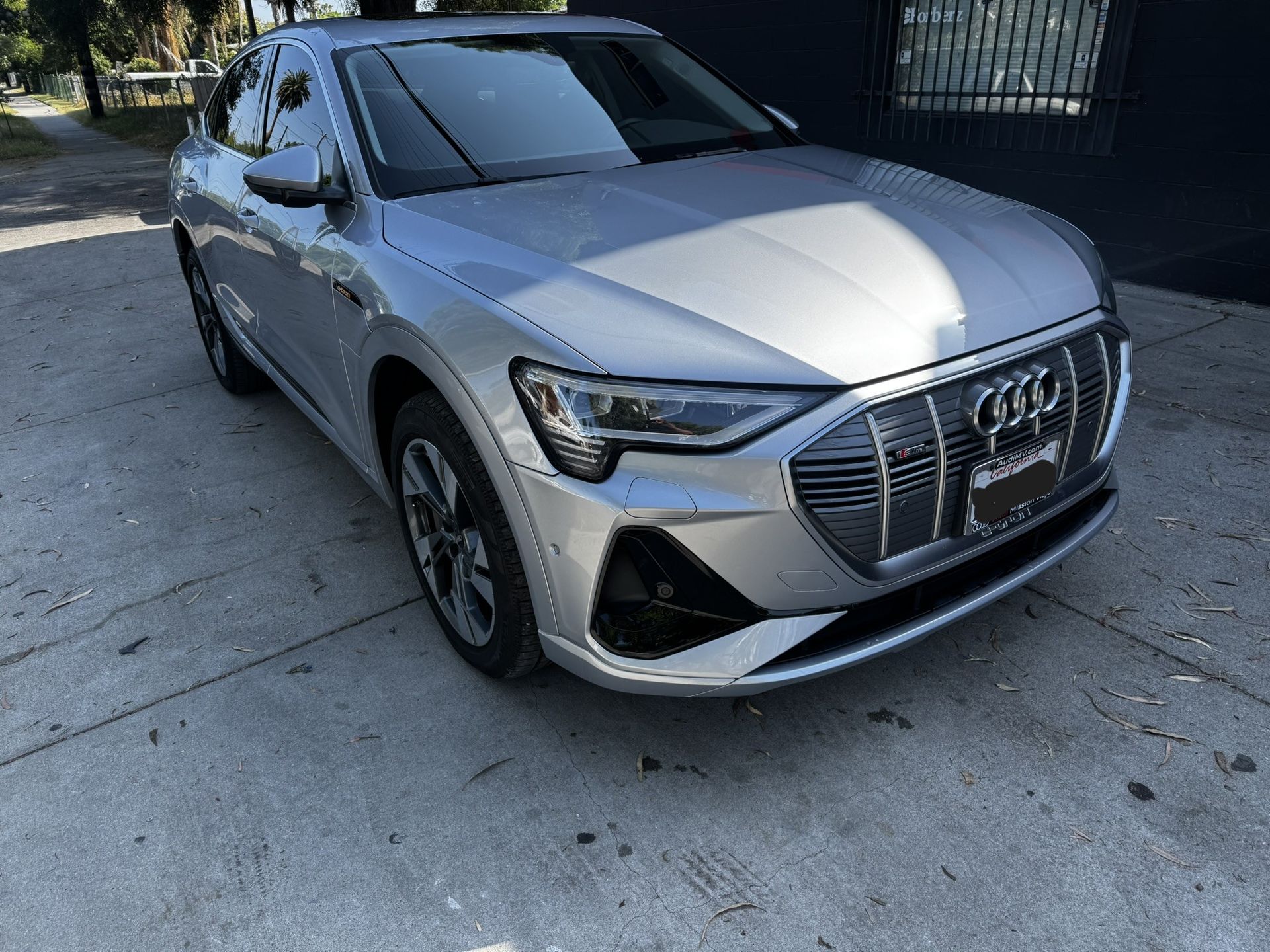 Silver Audi e-tron electric SUV parked on a paved street in front of a building.