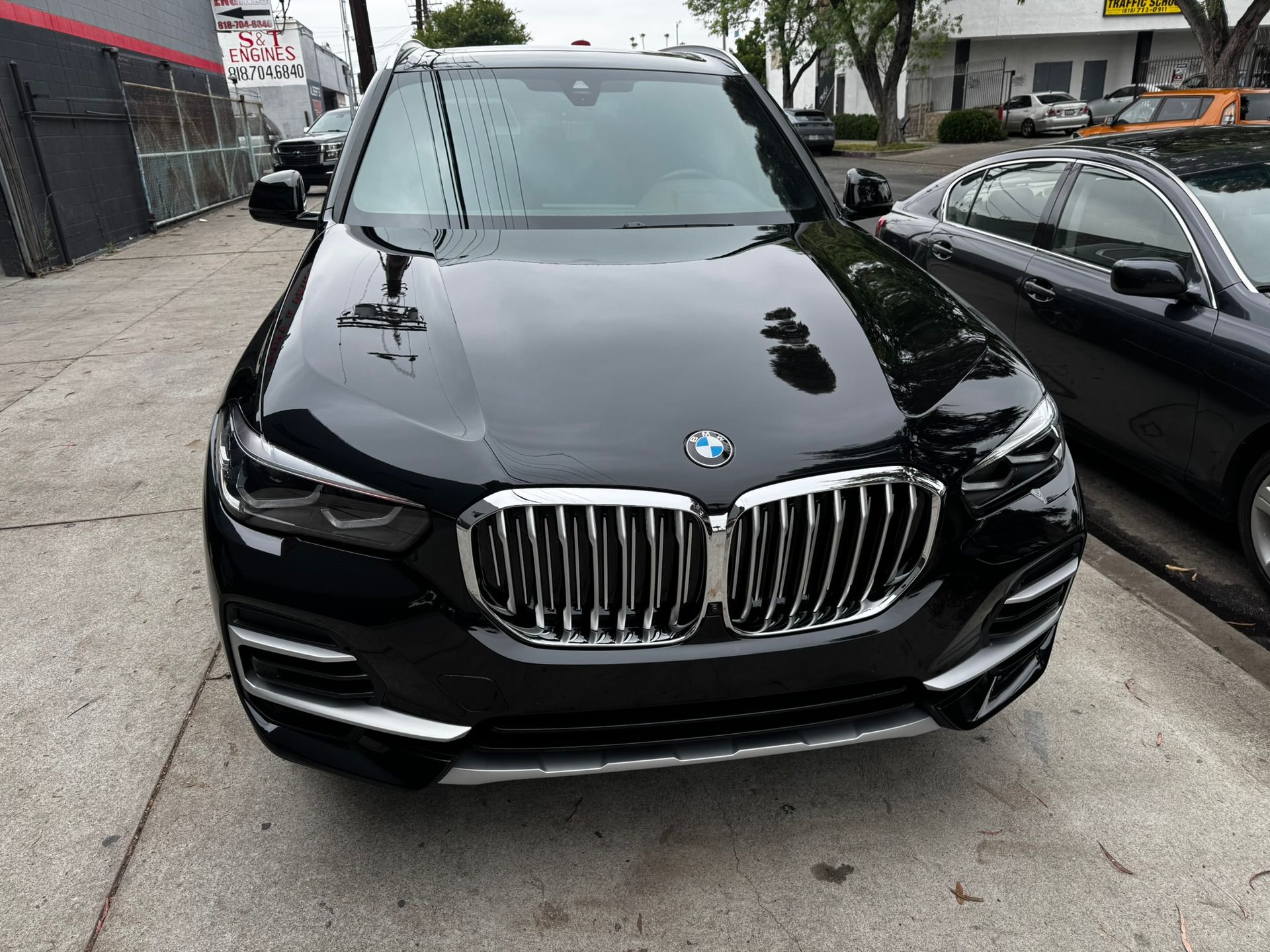 Black BMW SUV parked on the street. Reflective surface, chrome grill, next to a black sedan.