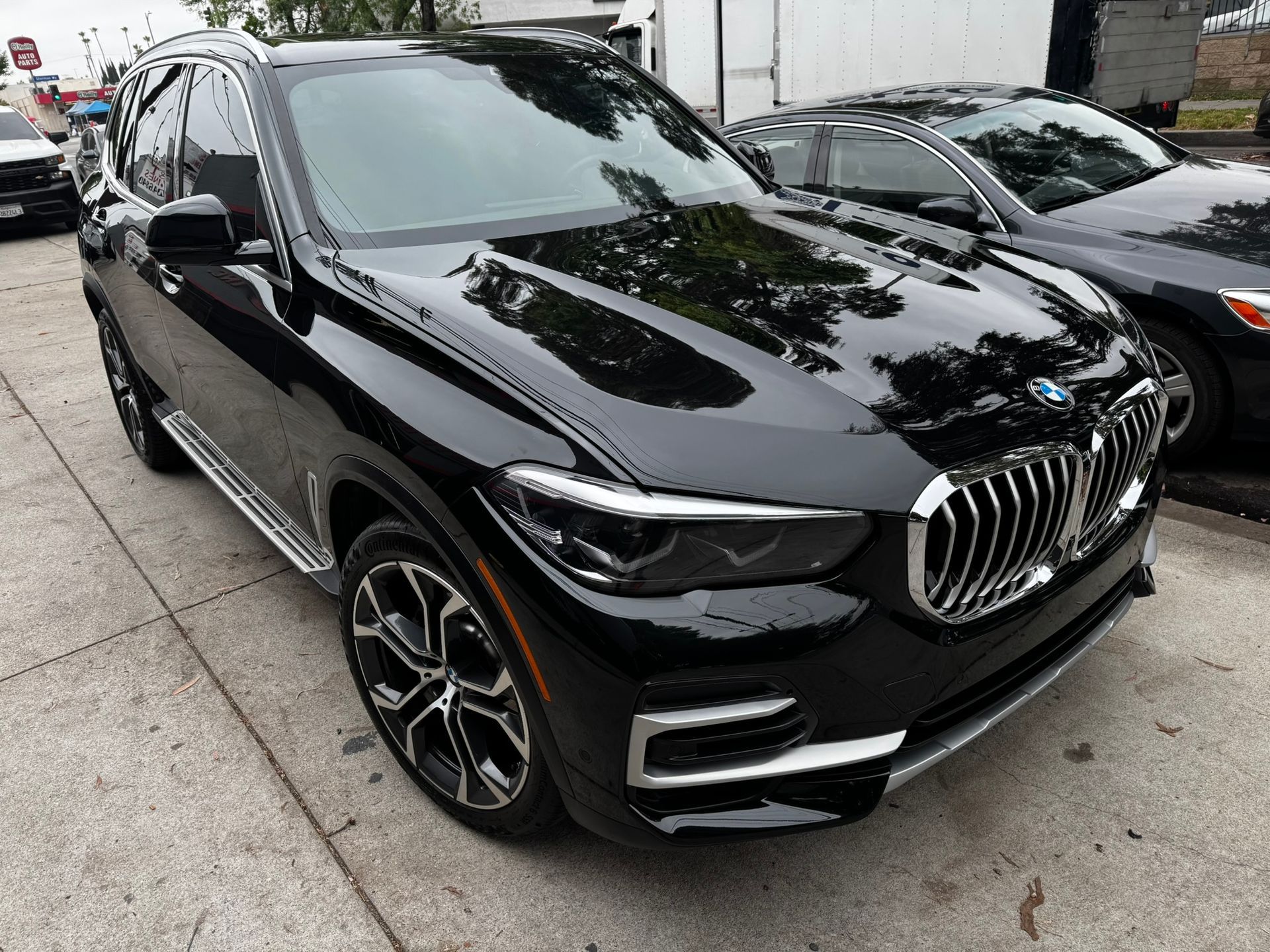Black BMW X5 SUV parked on a city street, reflecting sunlight.