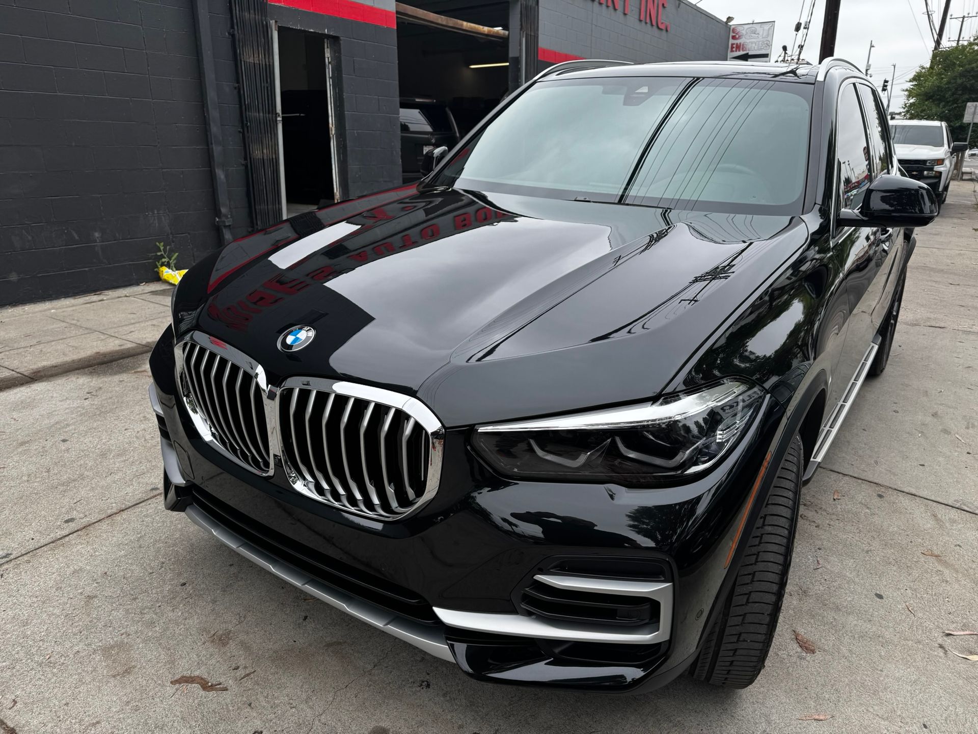 Black BMW X5 parked in front of a building with chrome grill and headlights, sunny day.