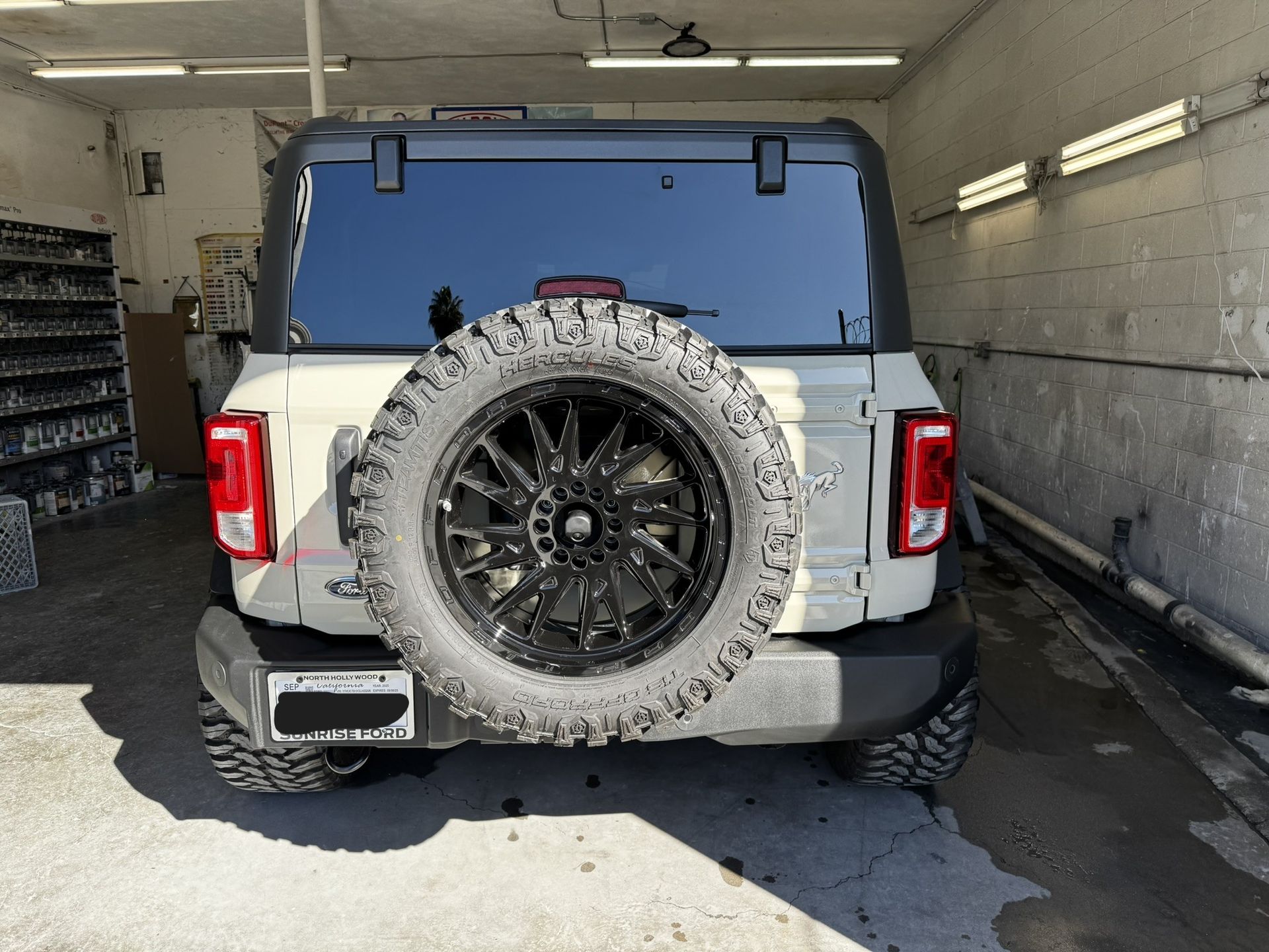 White Ford Bronco with black spare tire in a garage.