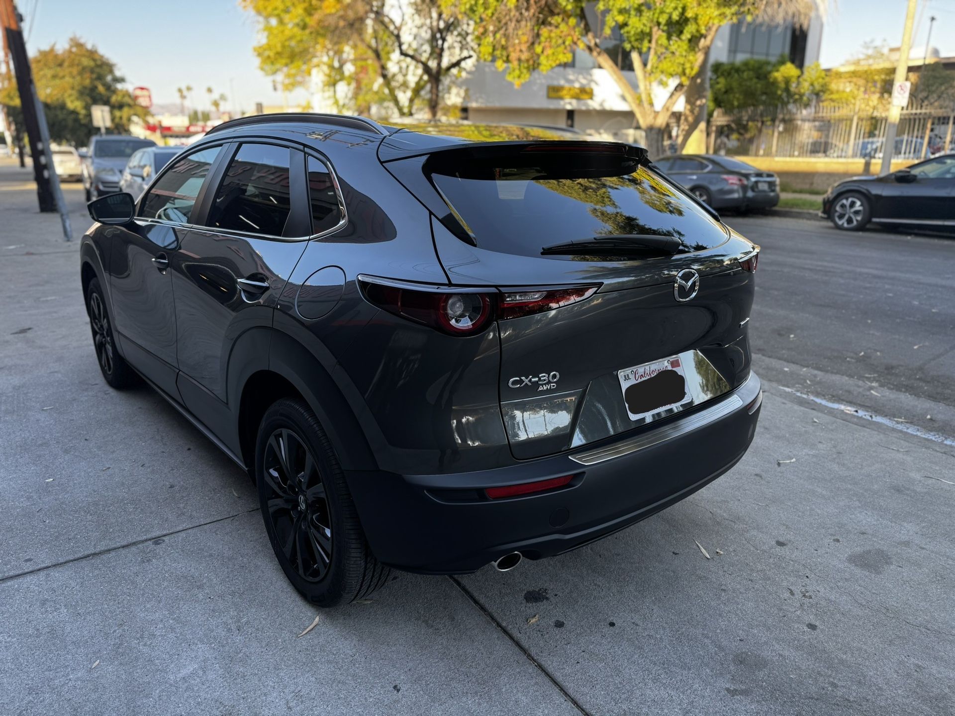 Dark gray Mazda CX-30 parked on a city street. Black wheels and trim. Clear, sunny day.