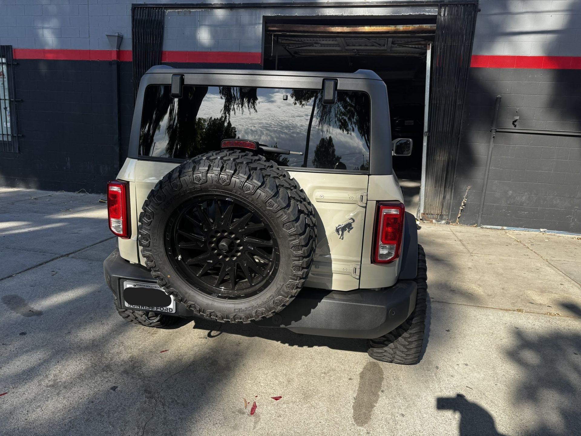 Tan Ford Bronco SUV with a spare tire on a city street.