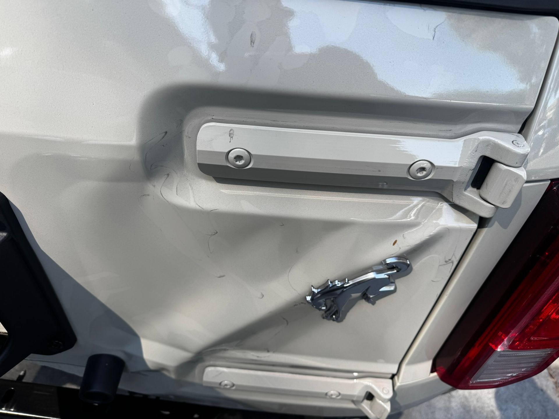 Close-up of a white car's rear, showing the door handle and a bent silver emblem.