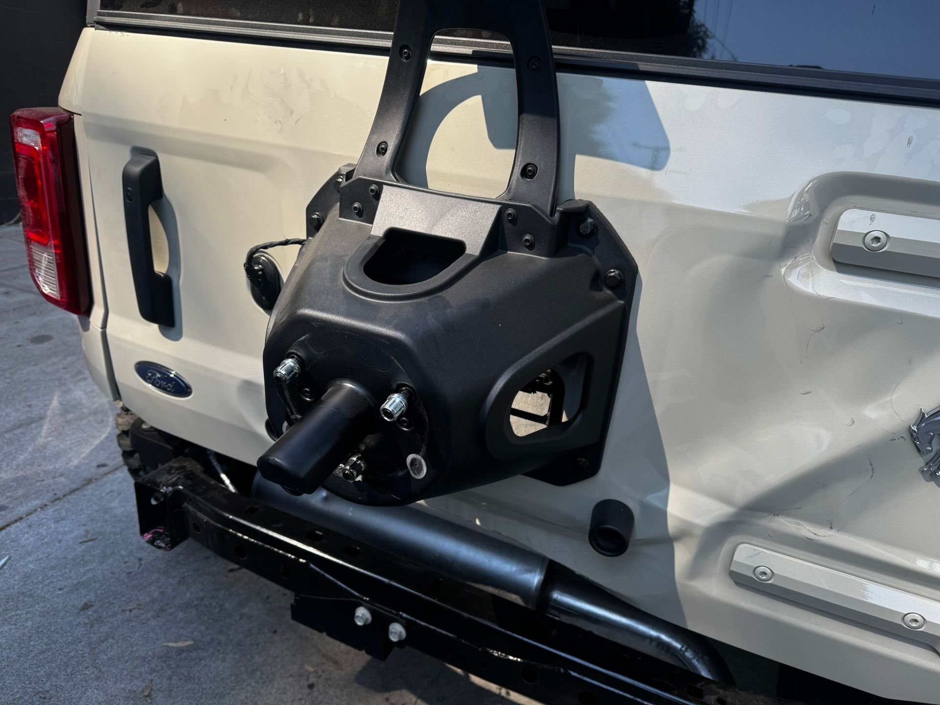Rear of beige Ford Bronco with a black spare tire carrier mounted on the back.