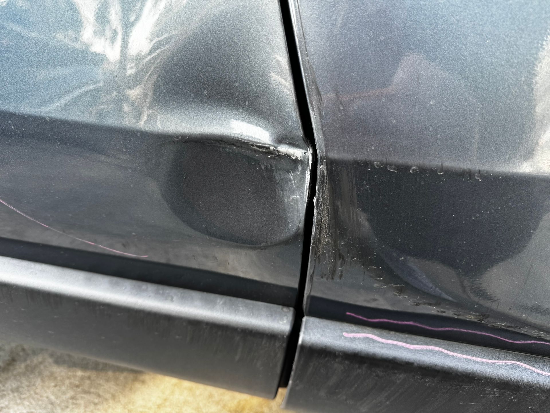 Damaged grey car door, dented and scratched, next to another car panel.