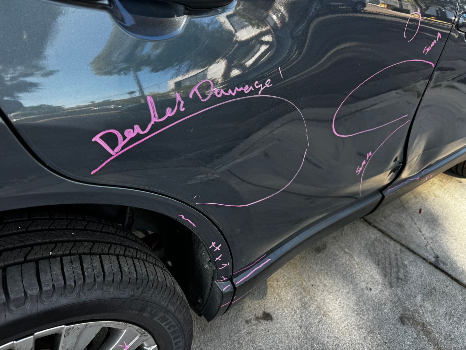 Dark gray car with pink markings indicating dents and scratches. Text reads 