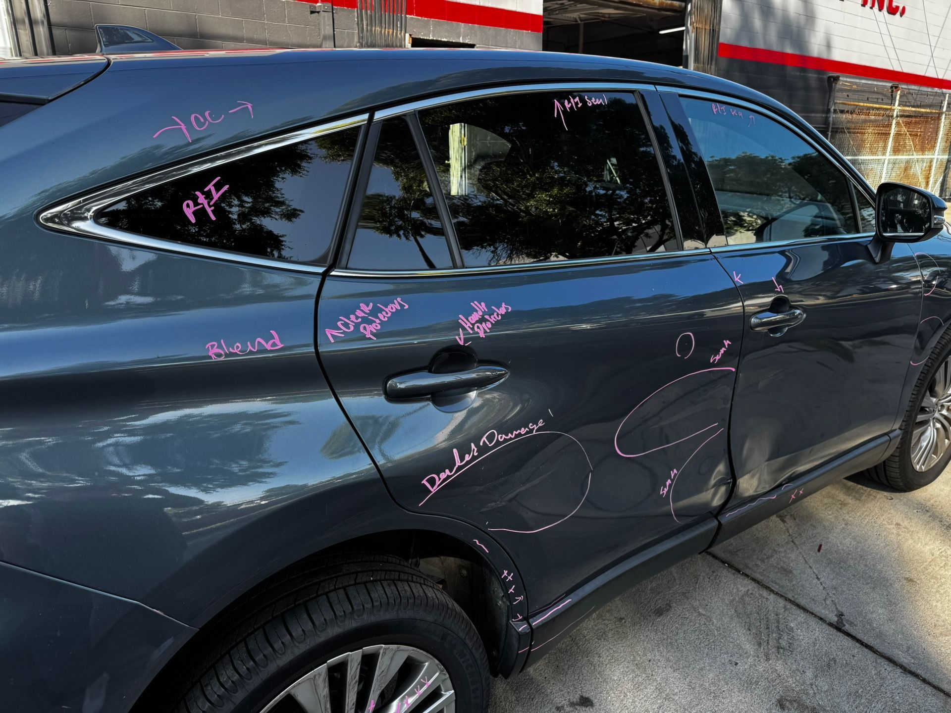 Dark gray car with pink writing on the side and windows, parked outside.