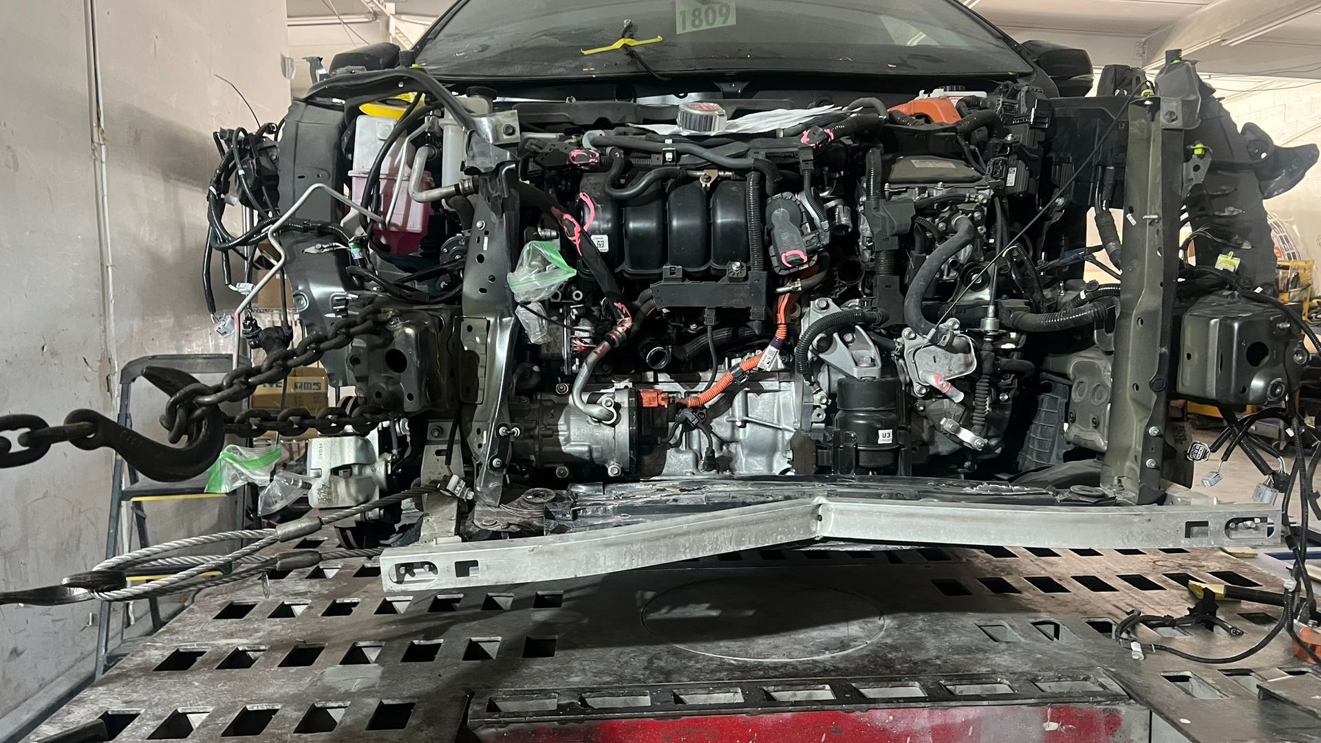 Severely damaged car chassis on a lift; engine and components exposed.