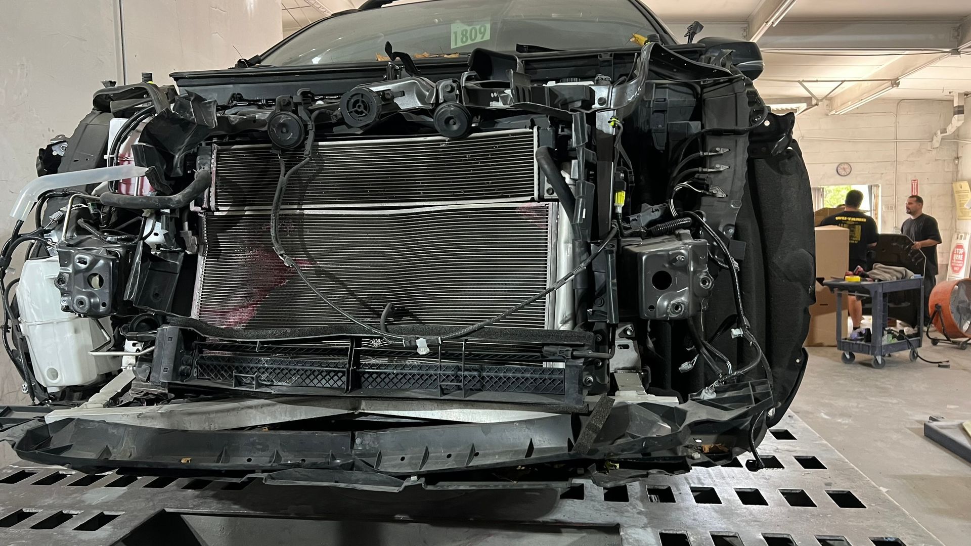 Damaged car front end in a repair shop, revealing engine components.