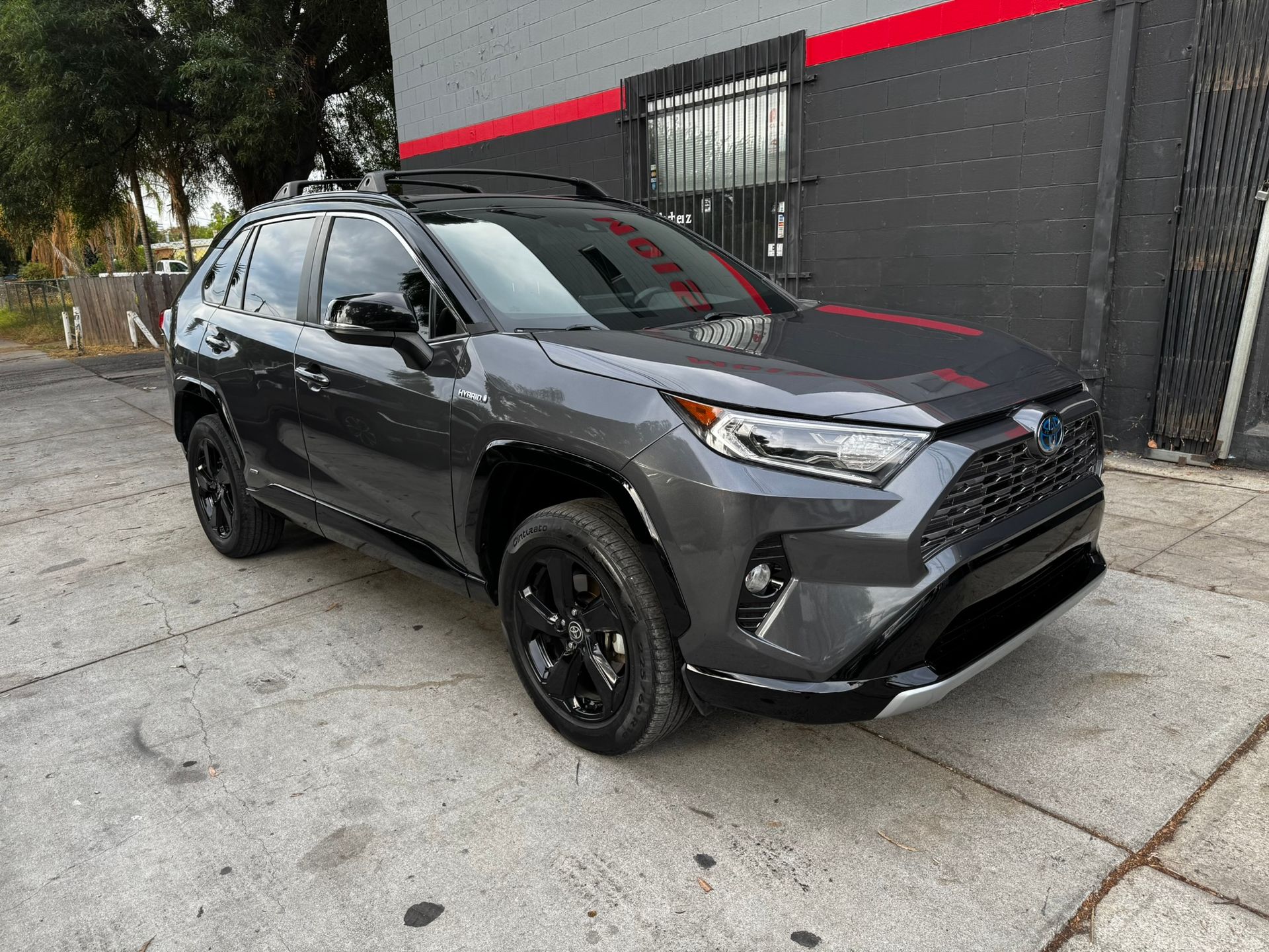 Gray Toyota RAV4 SUV with black wheels parked in front of a building with red and black accents.