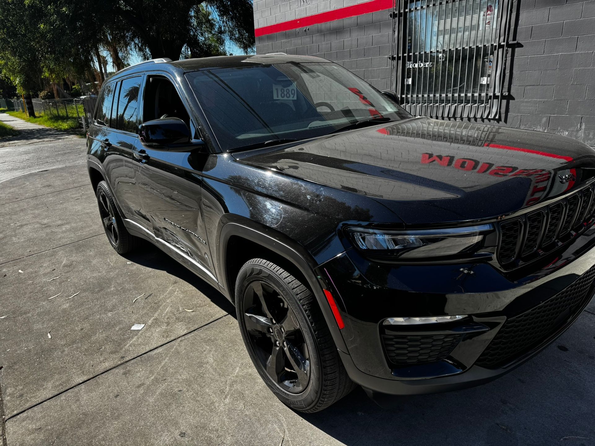 Black Jeep Grand Cherokee parked on a city street in front of a building with a red sign.