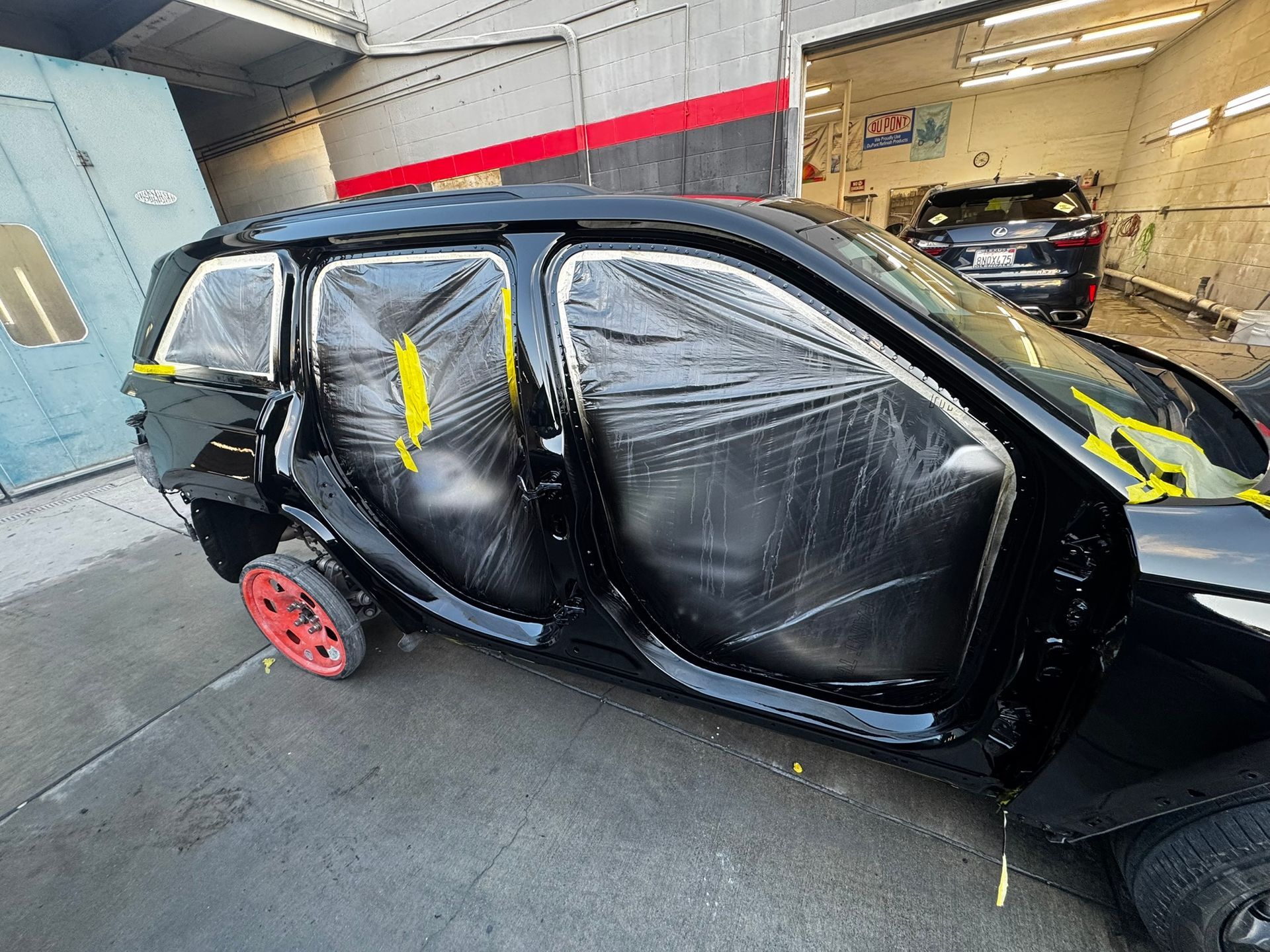 Black car in a paint booth, covered in plastic and tape, ready for paintwork.