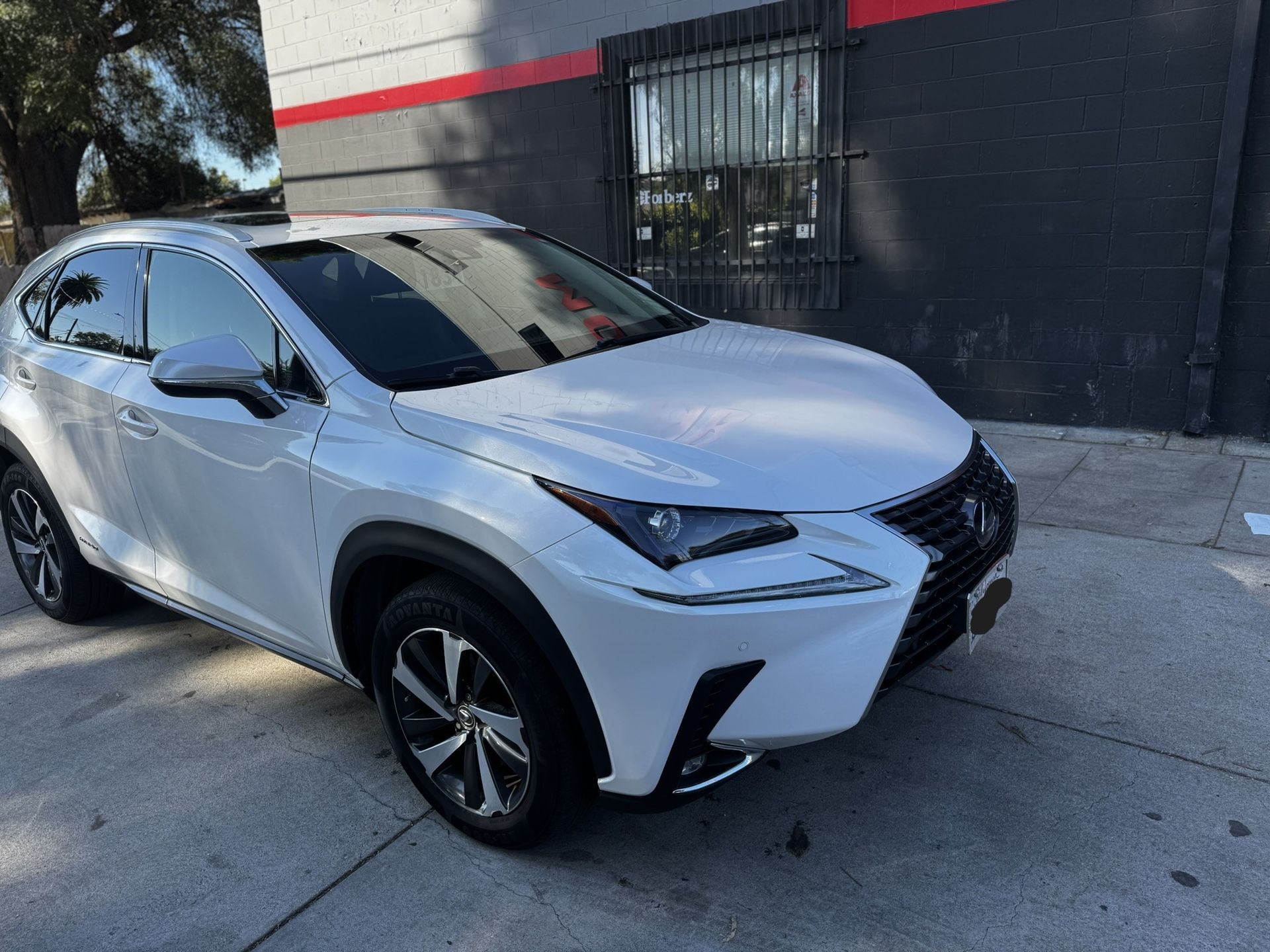White Lexus NX SUV parked in front of a building with a black and red facade.