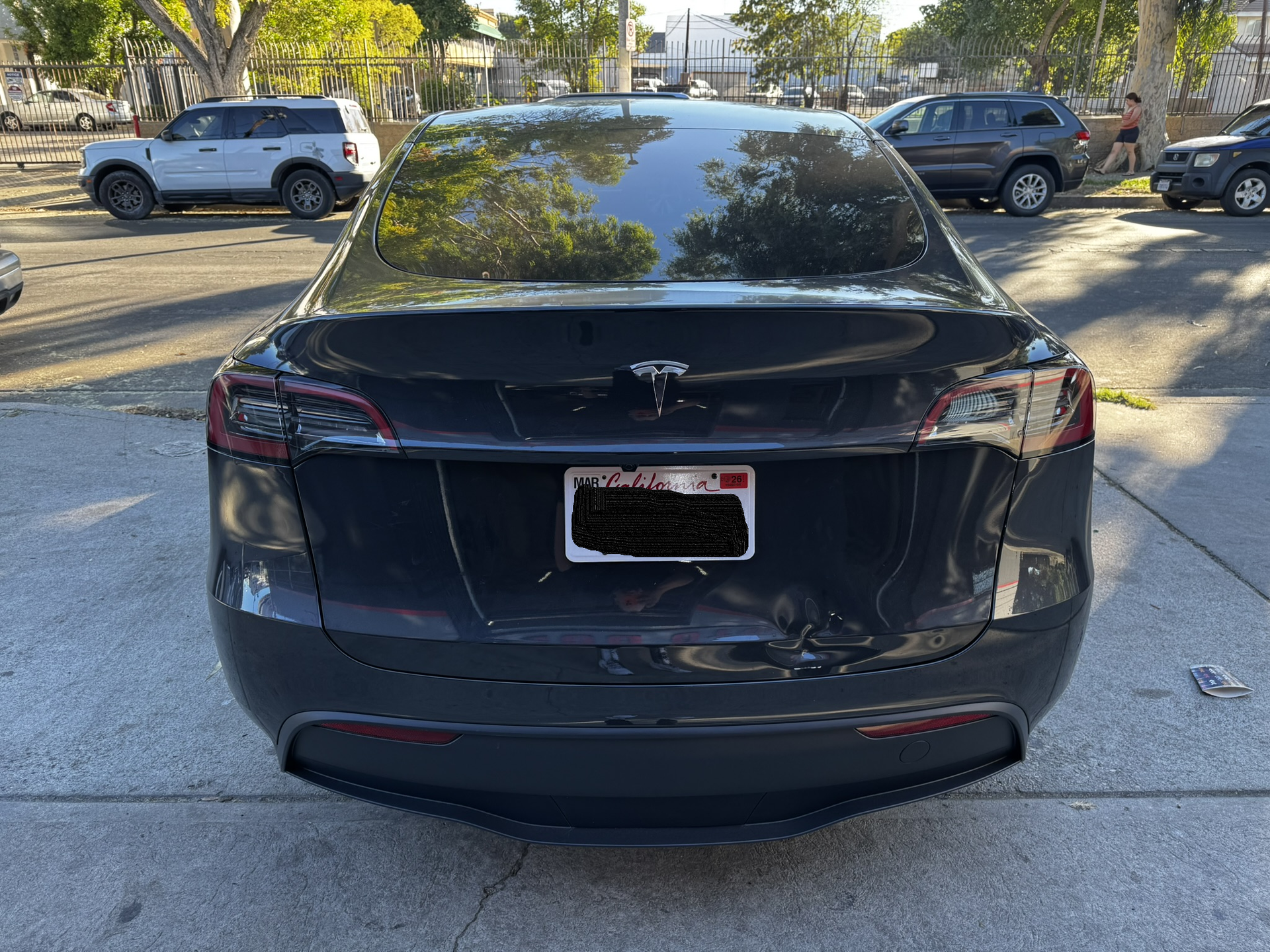 Dark gray Tesla sedan, rear view, in parking lot, with visible damage to the rear.
