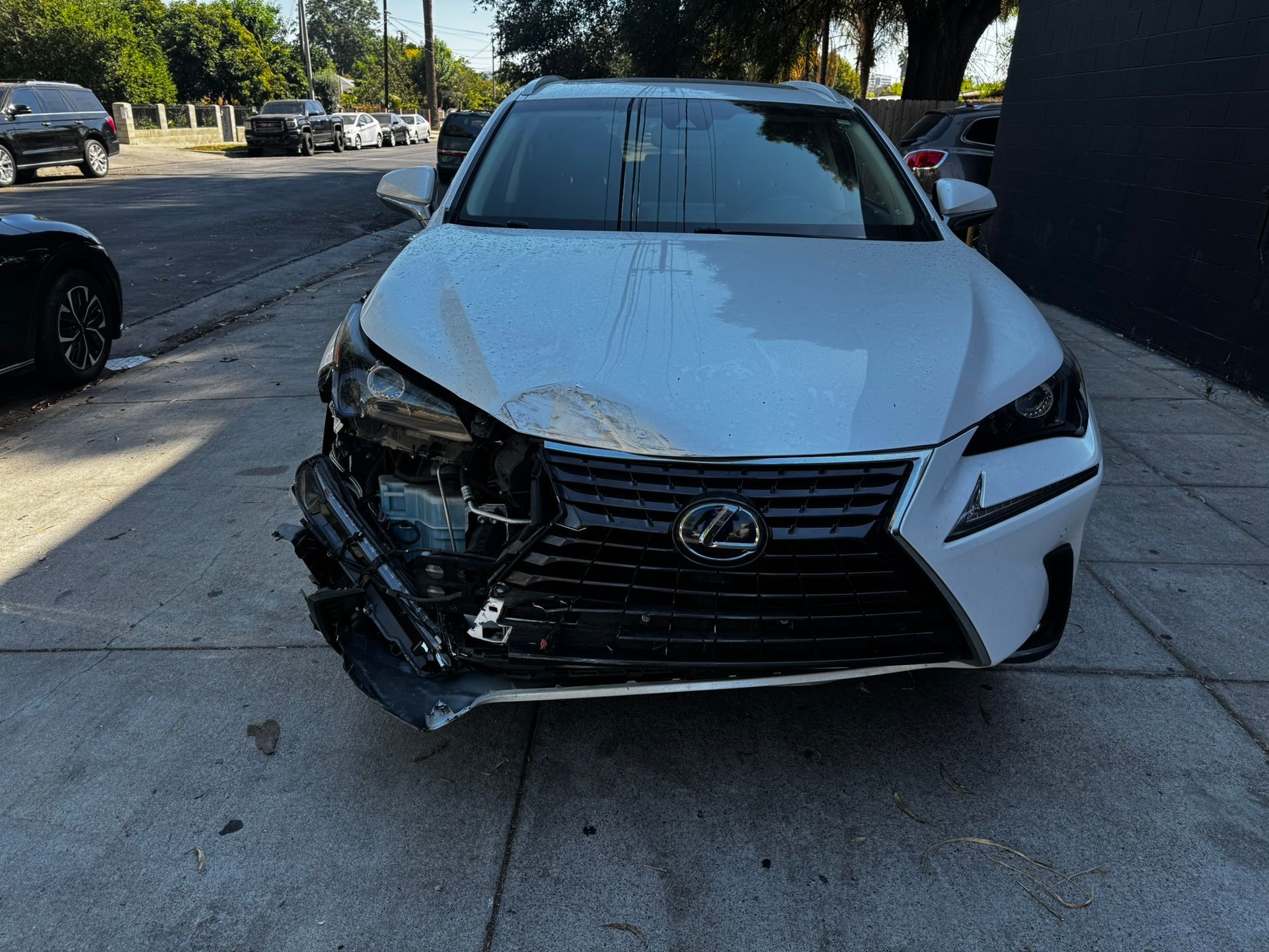 White Lexus SUV with severe front-end damage parked on a sidewalk next to a street.