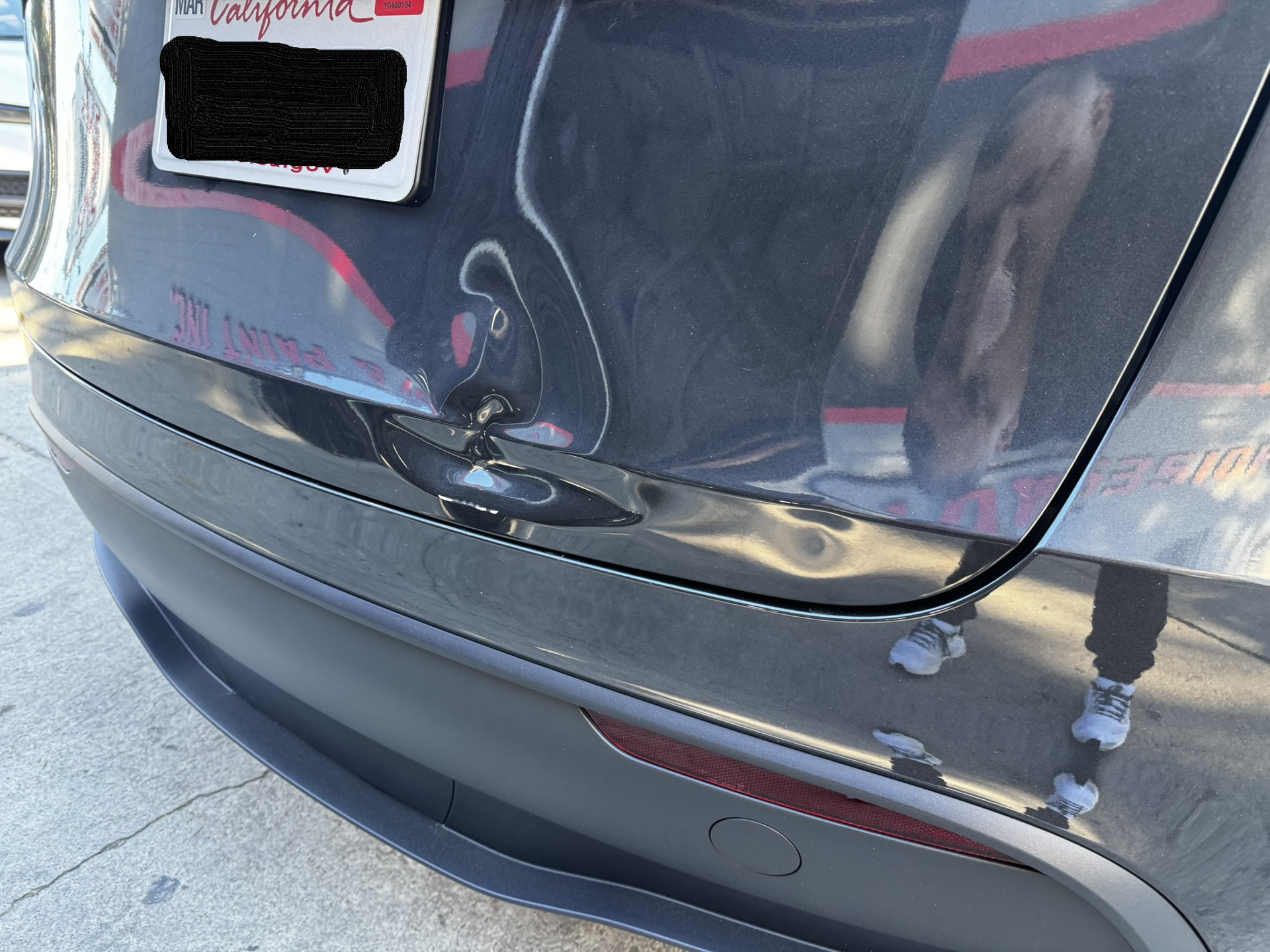 Damaged gray car bumper with a dent near a black sensor. License plate visible.